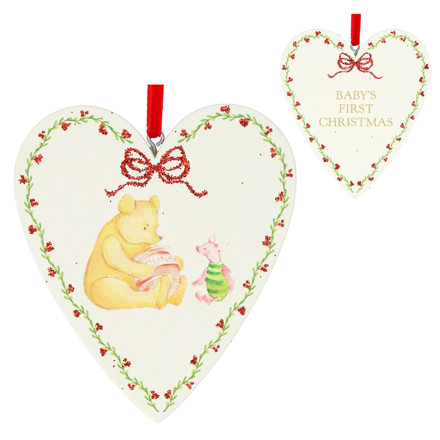 Heart-shaped Christmas ornament featuring Winnie the Pooh and Piglet, with a red ribbon hanger and a smaller matching ornament in the background showing the text 'BABY'S FIRST CHRISTMAS'.