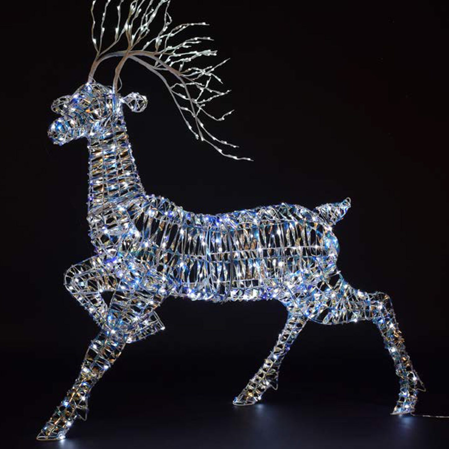 A lit festive deer sculpture with iridescent panels and metal frame, with branching antlers and glowing white lights, shown against a black background.