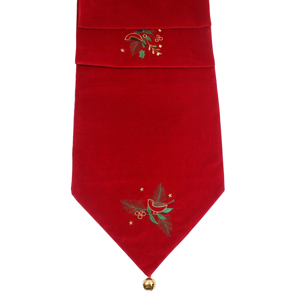 A red velvet Christmas table runner with embroidered holiday motifs, including a bird, pine branches, berries, and stars, shown against a plain white background.