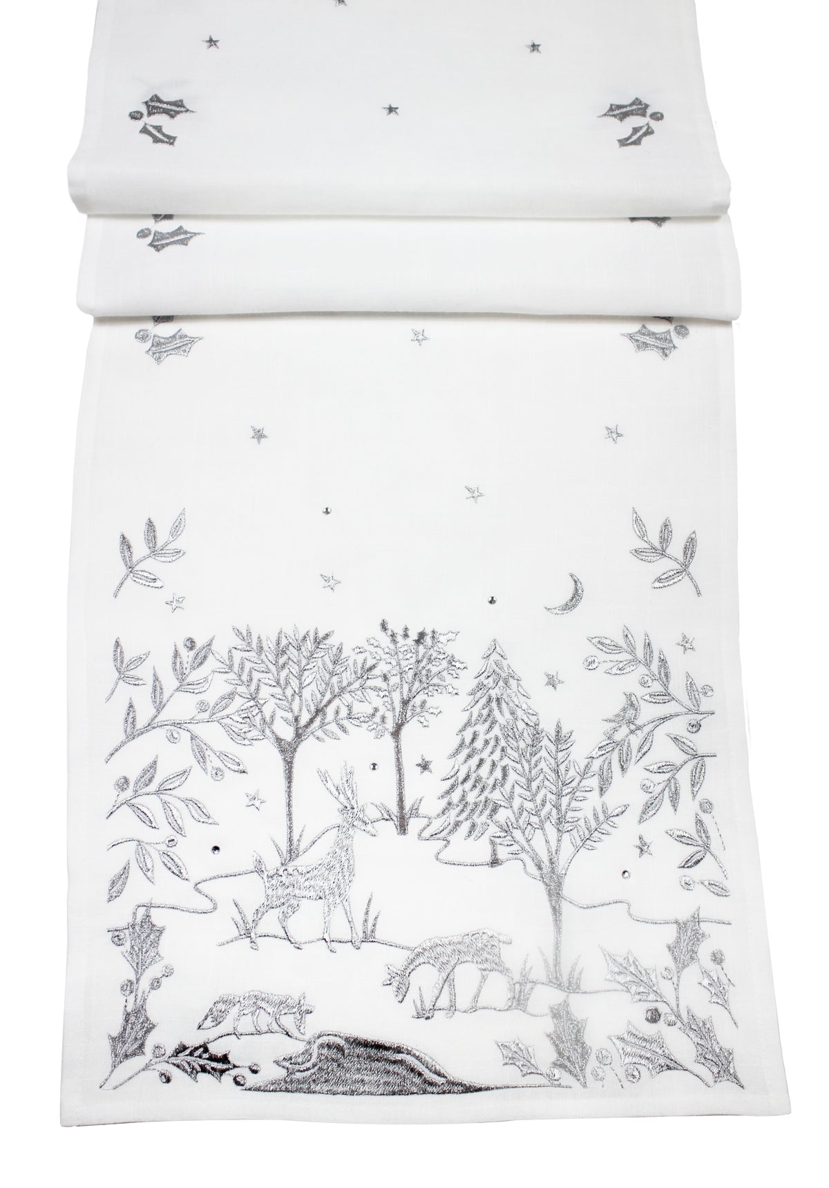 A white fabric table runner, featuring a delicate silver embroidered woodland scene with trees, deer, stars, and a crescent moon.