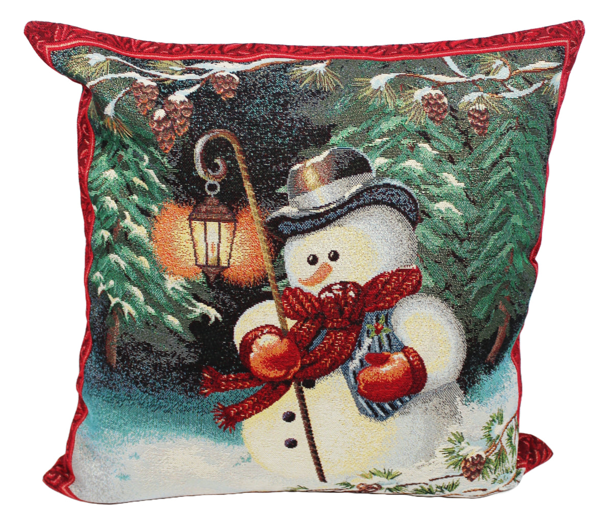A square decorative throw pillow featuring a festive needlepoint-style winter scene with a snowman wearing a red scarf and hat, surrounded by pine trees, snow, and a glowing lantern. The pillow has a red piped border and is shown against a plain white background.