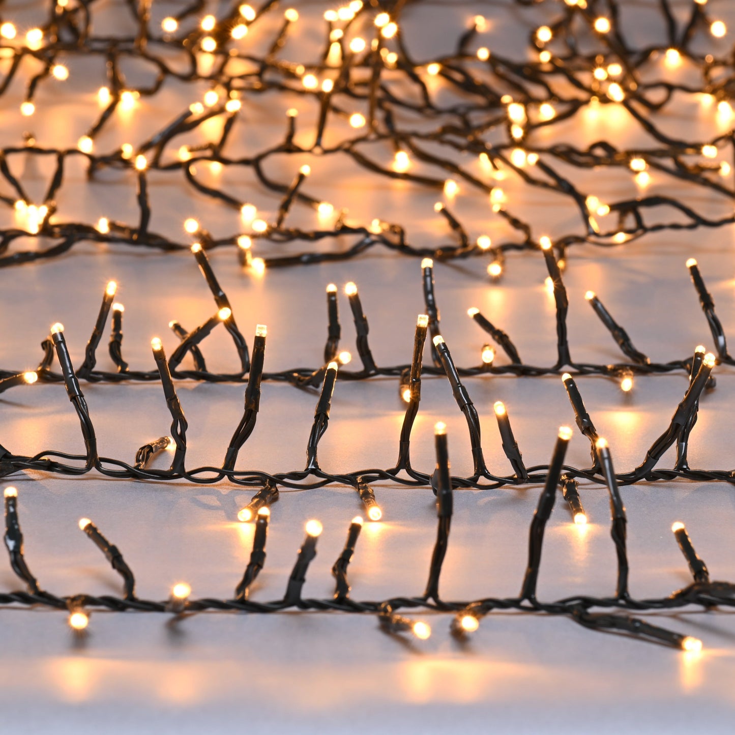 A close-up image of Festive 1000 Traditional Warm White Firefly Christmas Cluster Lights, showing the twinkle of the lights against a black cable.