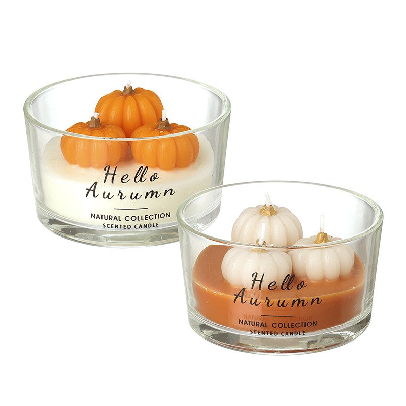 Two glass scented candles labelled 'Hello Autumn' in the Natural Collection, shown on a white background. One candle has orange pumpkins on top, and the other has white pumpkins on top.