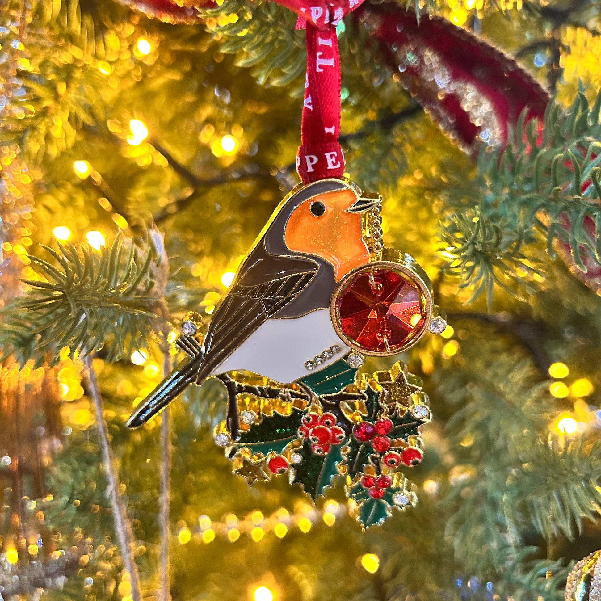 Decorative Christmas ornament of a robin with holly berries on a tree.