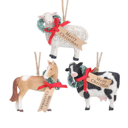 Three Christmas hanging ornaments shaped like a white sheep, a tan horse, and a black-and-white cow, each decorated with a green wreath, red ribbon, twine loop, and a small paper tag that reads Merry Christmas, shown on a white background.