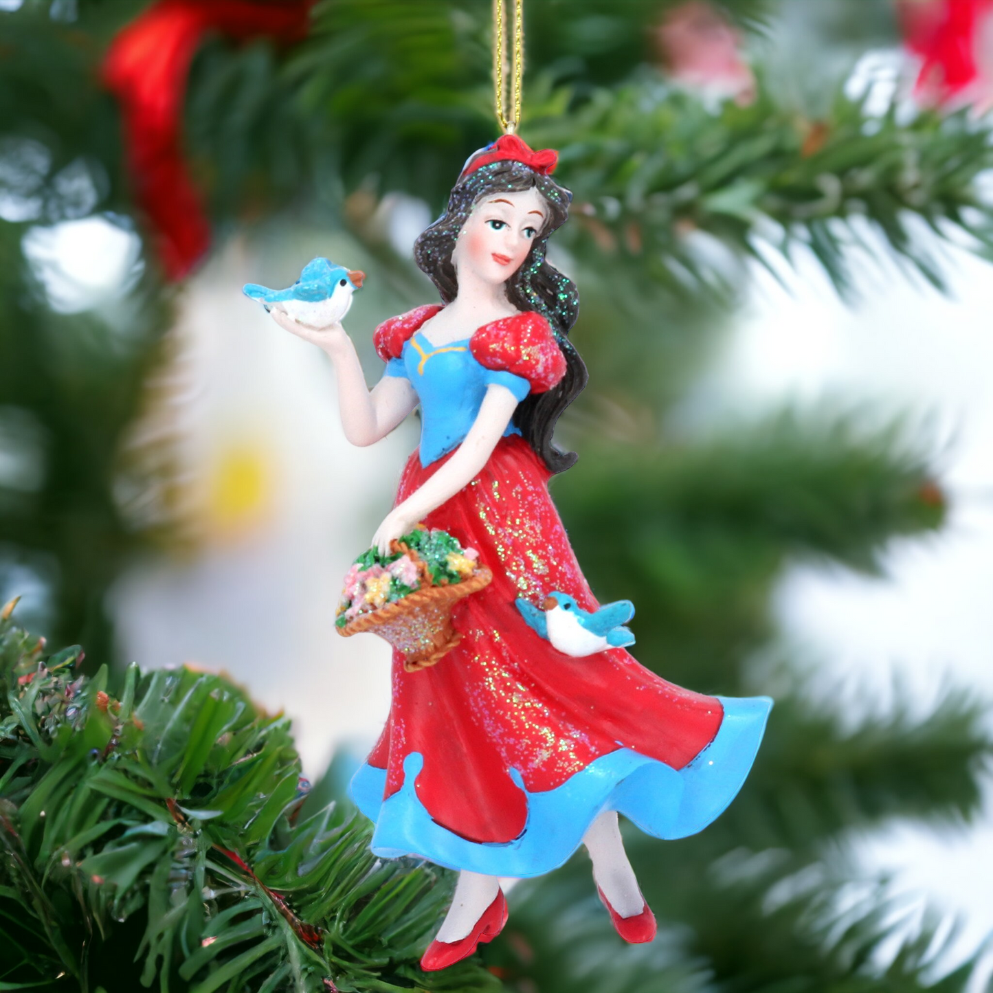 A resin figurine of Snow White holding a basket, with a red and blue dress, standing on a green Christmas tree. The background includes other Christmas decorations.