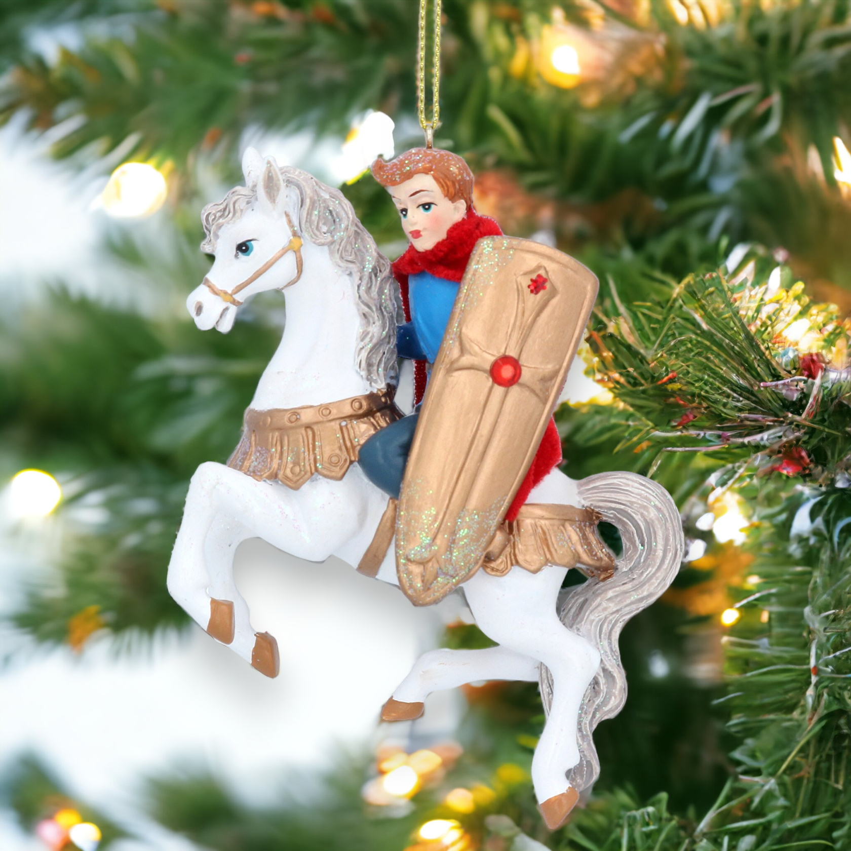 A hanging Christmas tree decoration featuring a resin figurine of a prince riding a horse, dressed in gold and red attire, with a white horse, against a backdrop of festive holiday lights and greenery.