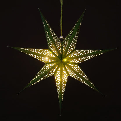 A glowing seven-pointed star hanging ornament made of green paper with intricate cutout patterns, emitting a warm yellow light against a solid black background.