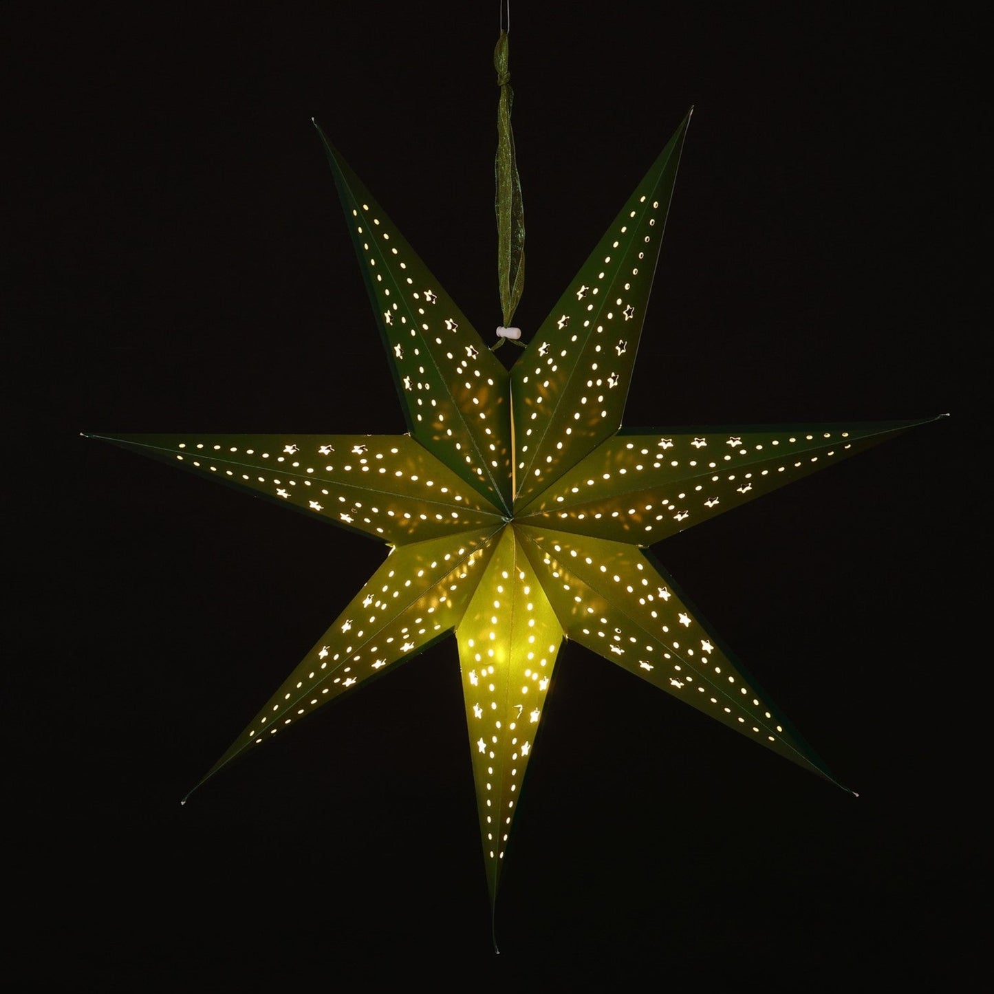 A glowing seven-pointed paper star Christmas ornament with small illuminated dots along its edges, hanging against a solid black background.