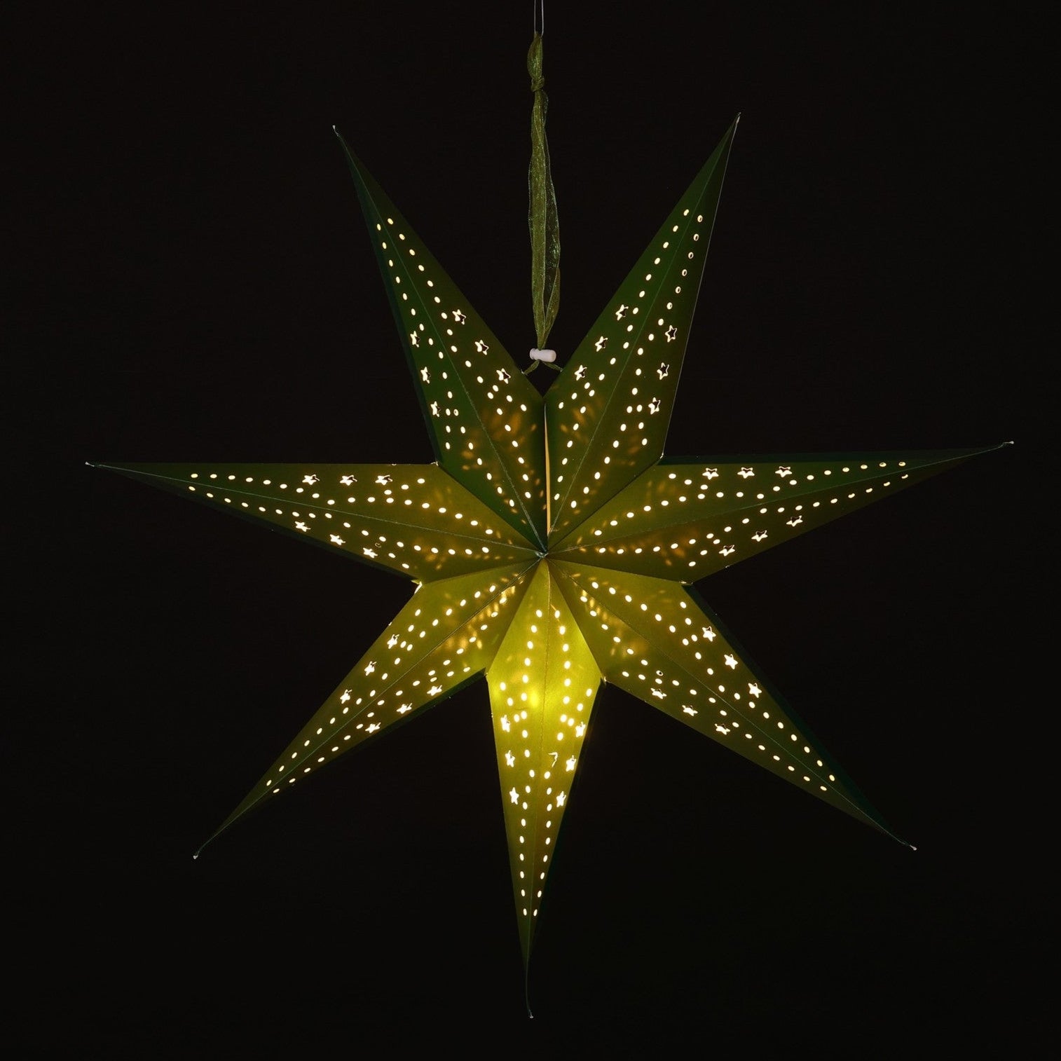 A glowing seven-pointed paper star Christmas ornament with small illuminated dots along its edges, hanging against a solid black background.