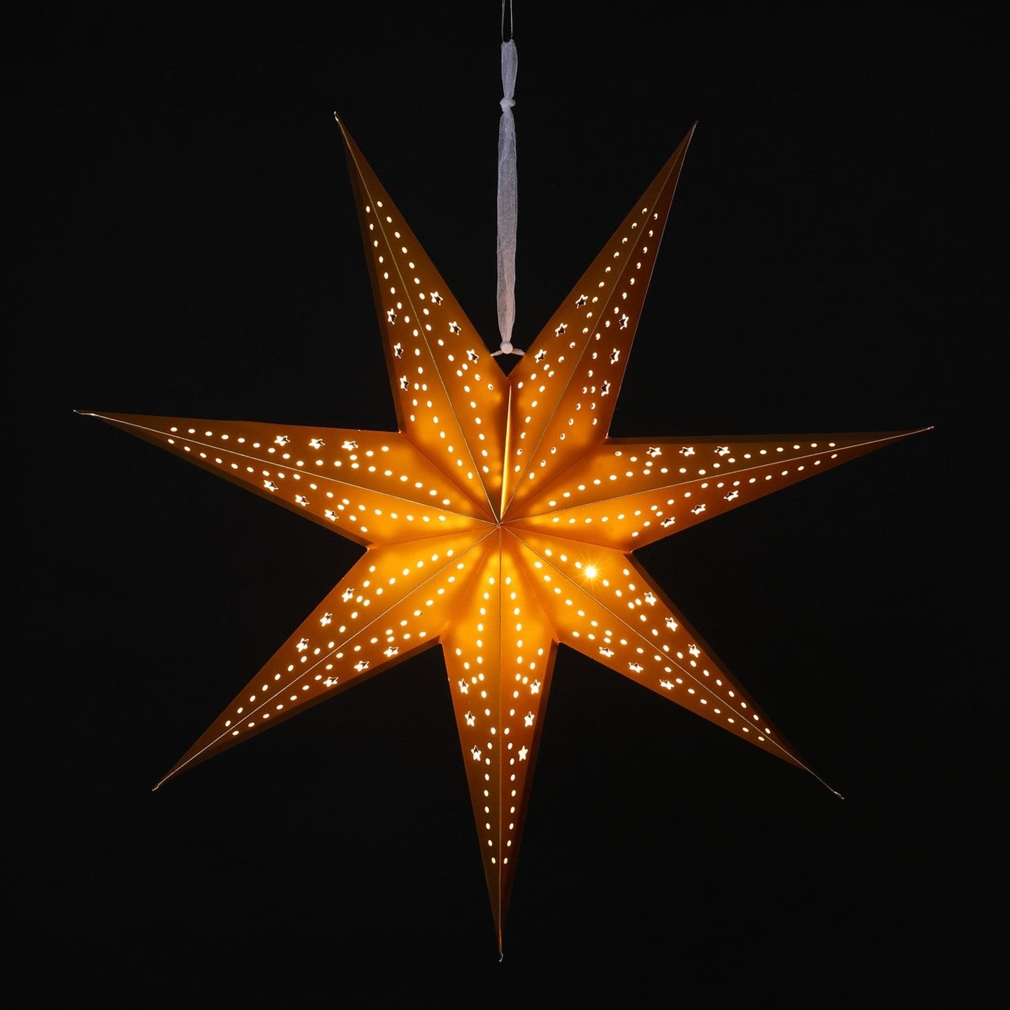 A glowing seven-pointed star Christmas ornament with small cutout windows, suspended by a white string against a solid black background.