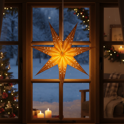 A glowing nine-pointed star Christmas ornament with embedded warm lights hangs in front of a dark wood window, with a snowy outdoor scene and cozy indoor holiday decor visible in the background.
