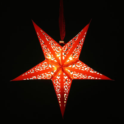 A red five-pointed star-shaped hanging ornament with intricate cutout patterns, glowing with warm light against a solid black background.
