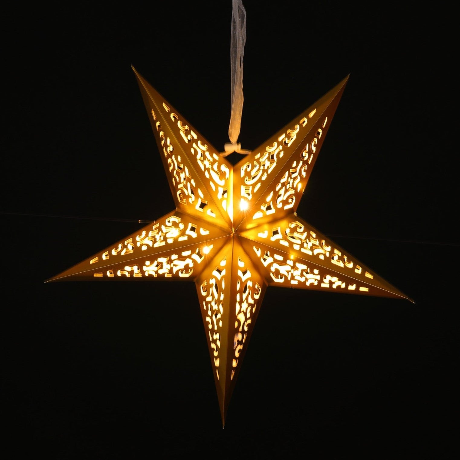 A glowing five-pointed star hanging ornament with intricate cutout patterns, emitting a warm golden light against a solid black background.