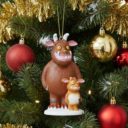 A Christmas ornament shaped like the Gruffalo and its child hanging on a decorated Christmas tree with gold tinsel, red and gold baubles, and lights.