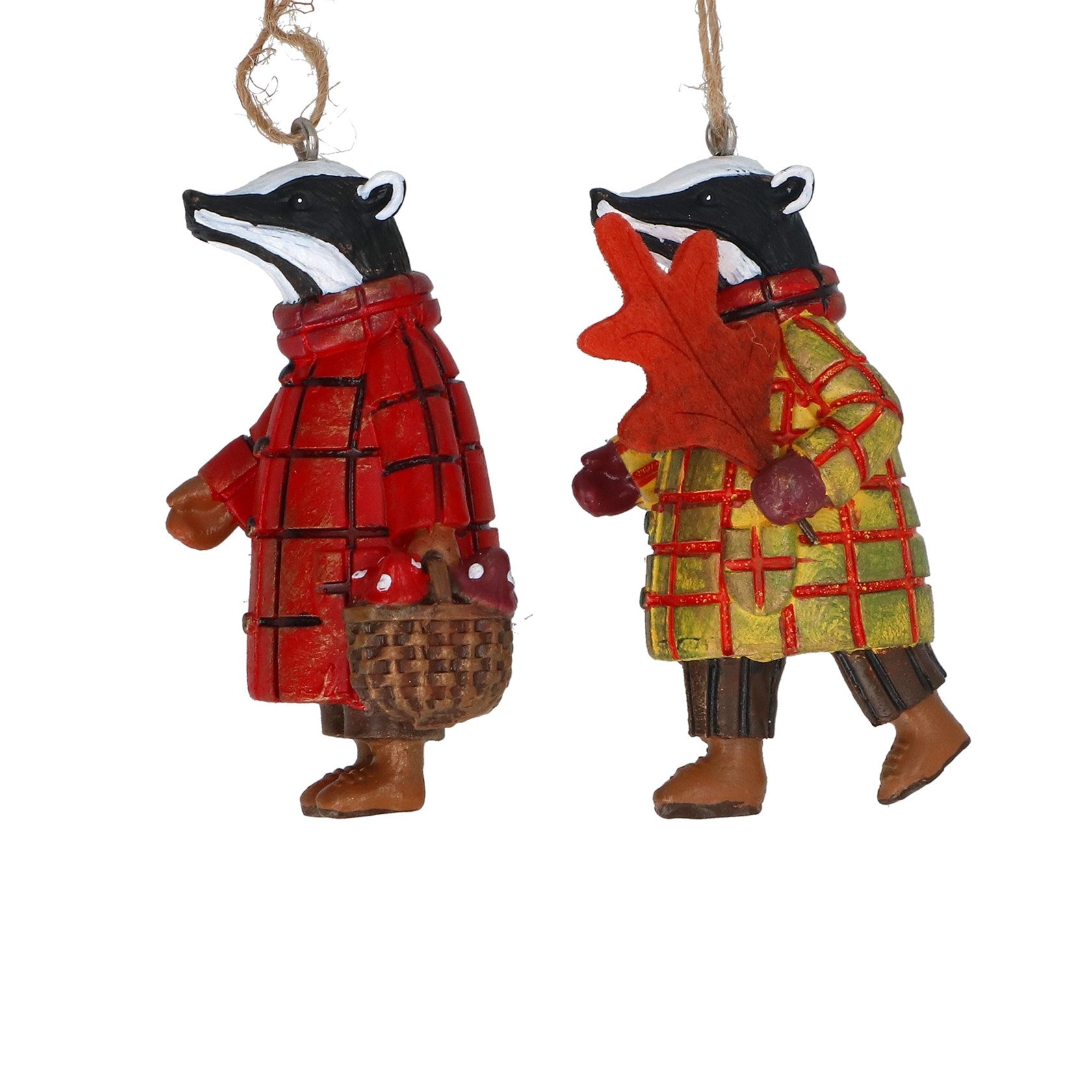 Two hanging badger ornaments dressed in autumn clothing, one in a red plaid coat holding a basket and one in a yellow-green plaid coat holding an orange leaf, on a white background.