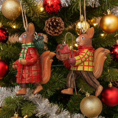 Two resin squirrel Christmas ornaments hanging on a decorated Christmas tree. One squirrel wears a red plaid coat and green scarf, and the other wears a yellow plaid coat and brown pants, both holding small red and green accents.