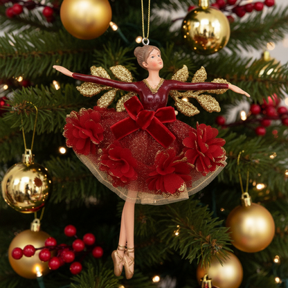 A ballerina Christmas ornament featuring a female dancer in a red tutu with red fabric flowers, gold glitter wings, and a gold hanging loop, shown on a Christmas tree background.
