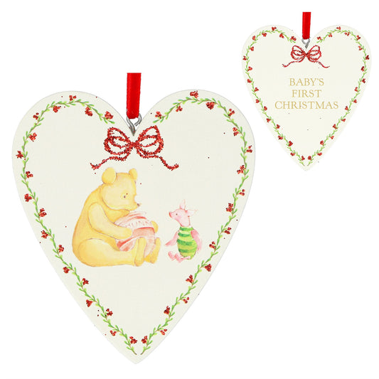 Heart-shaped Christmas ornament featuring Winnie the Pooh and Piglet, with a red ribbon hanger and a smaller matching ornament in the background showing the text 'BABY'S FIRST CHRISTMAS'.
