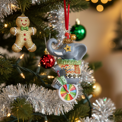 A gray elephant Christmas ornament riding a colorful unicycle with a patterned sweater, hanging on a decorated Christmas tree with silver tinsel and warm lights.