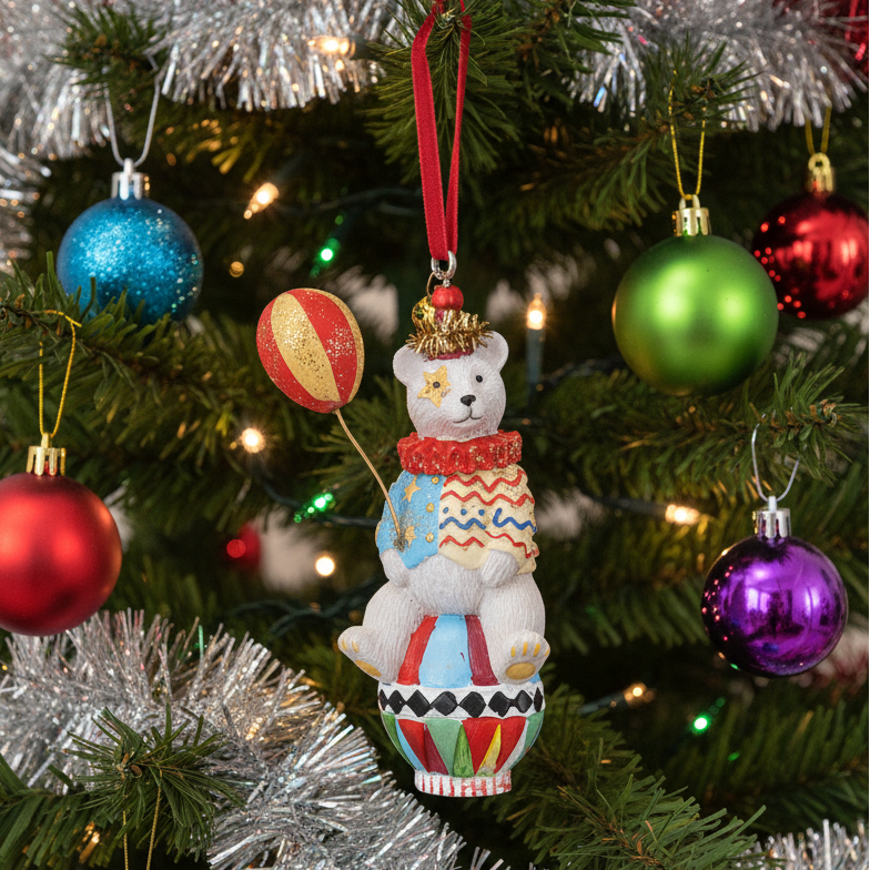 A white resin teddy bear Christmas ornament hanging on a decorated Christmas tree. The ornament features a colourful patterned outfit, a gold hat, and holds a red-and-gold striped balloon.