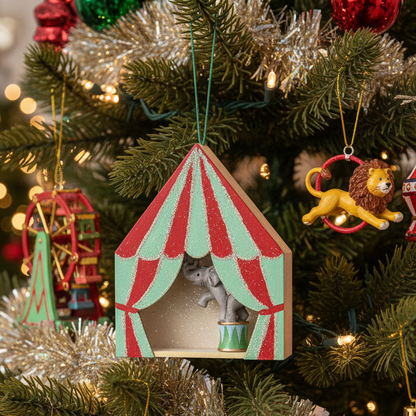 A miniature circus tent hanging ornament featuring a red and mint green striped circus tent design with glittery finish, a small grey elephant figurine inside, and a decorated drum on a light wood base.