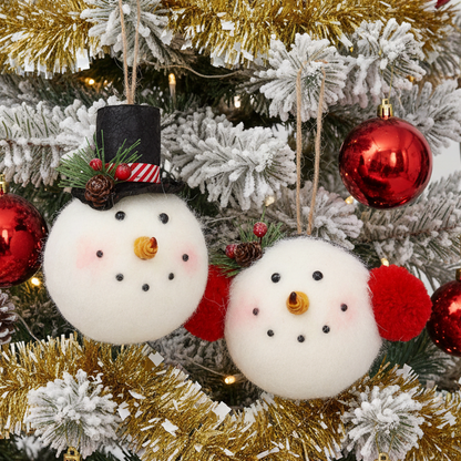 Two white felt snowman ornaments hanging on a decorated Christmas tree. One snowman wears a black top hat with red and white stripes and a small pinecone accent, while the second one has red pom-pom ears.