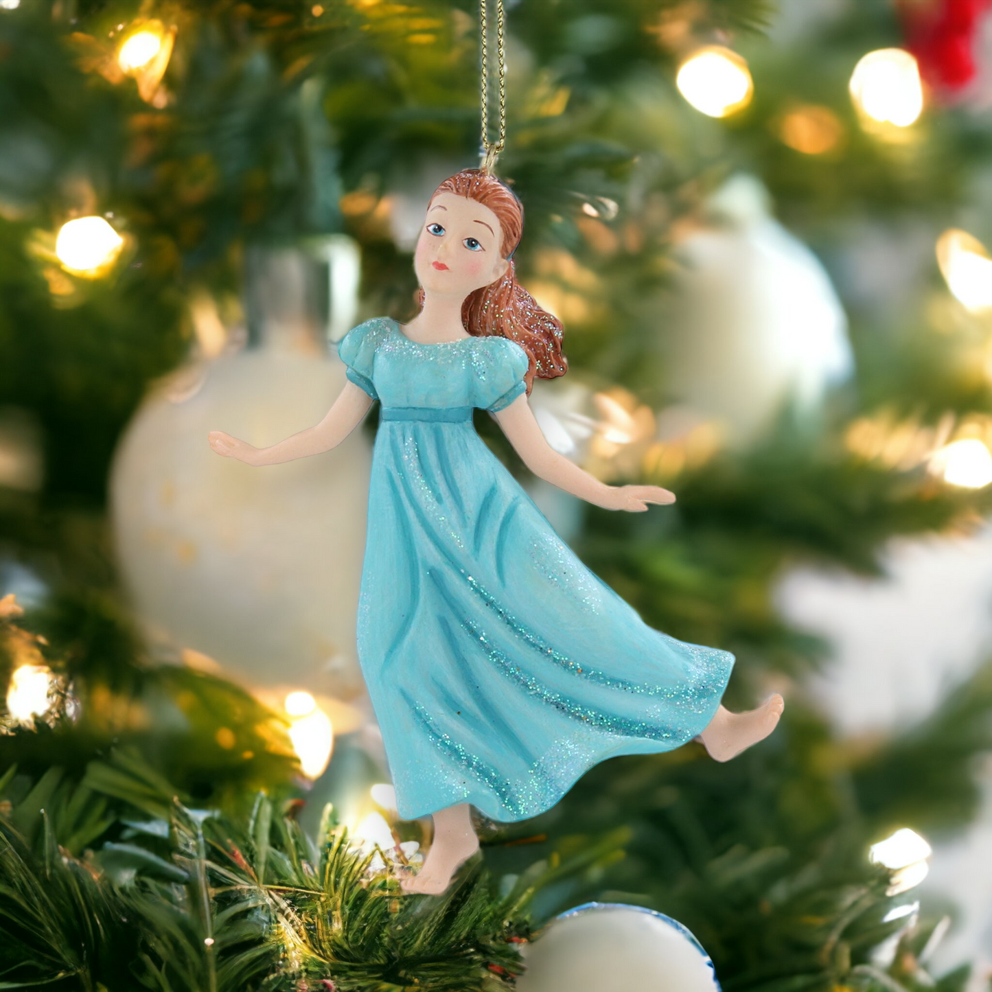 A resin figurine of the character Wendy from Peter Pan, in a blue dress with a sparkling gold hanging wire, placed on a Christmas tree.