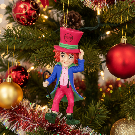 A whimsical Christmas ornament shaped like the Mad Hatter from Alice in Wonderland, hanging on a decorated Christmas tree. The ornament features a pink top hat with 'NO:18' printed on it, a blue coat, pink pants, and green boots, surrounded by festive red, gold, and green ornaments on a blurred background.