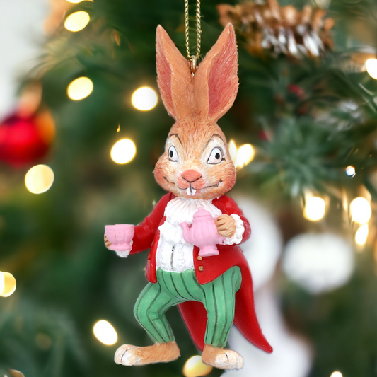 A decorative Mad March Hare figure in a red coat and green pants, holding a cup, hanging from a Christmas tree with blurred festive lights in the background.