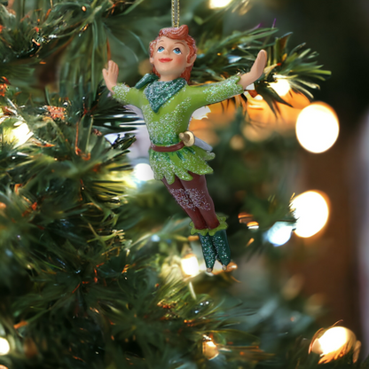 A resin figurine of Peter Pan hanging from a Christmas tree, with a green outfit and red hair, surrounded by golden lights.