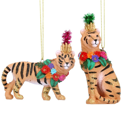 Two decorative tiger figurines with a Christmas theme, one standing and one sitting, adorned with colorful floral garlands and with gold hanging wires.
