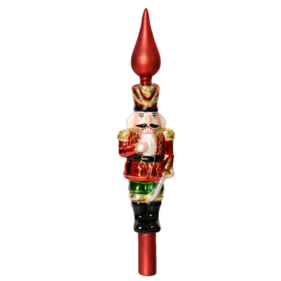 A glass finial nutcracker tree topper with a red hat, green jacket, and a white beard, set against a plain background.