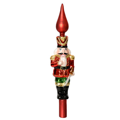 A glass finial nutcracker tree topper with a red hat, green jacket, and a white beard, set against a plain background.