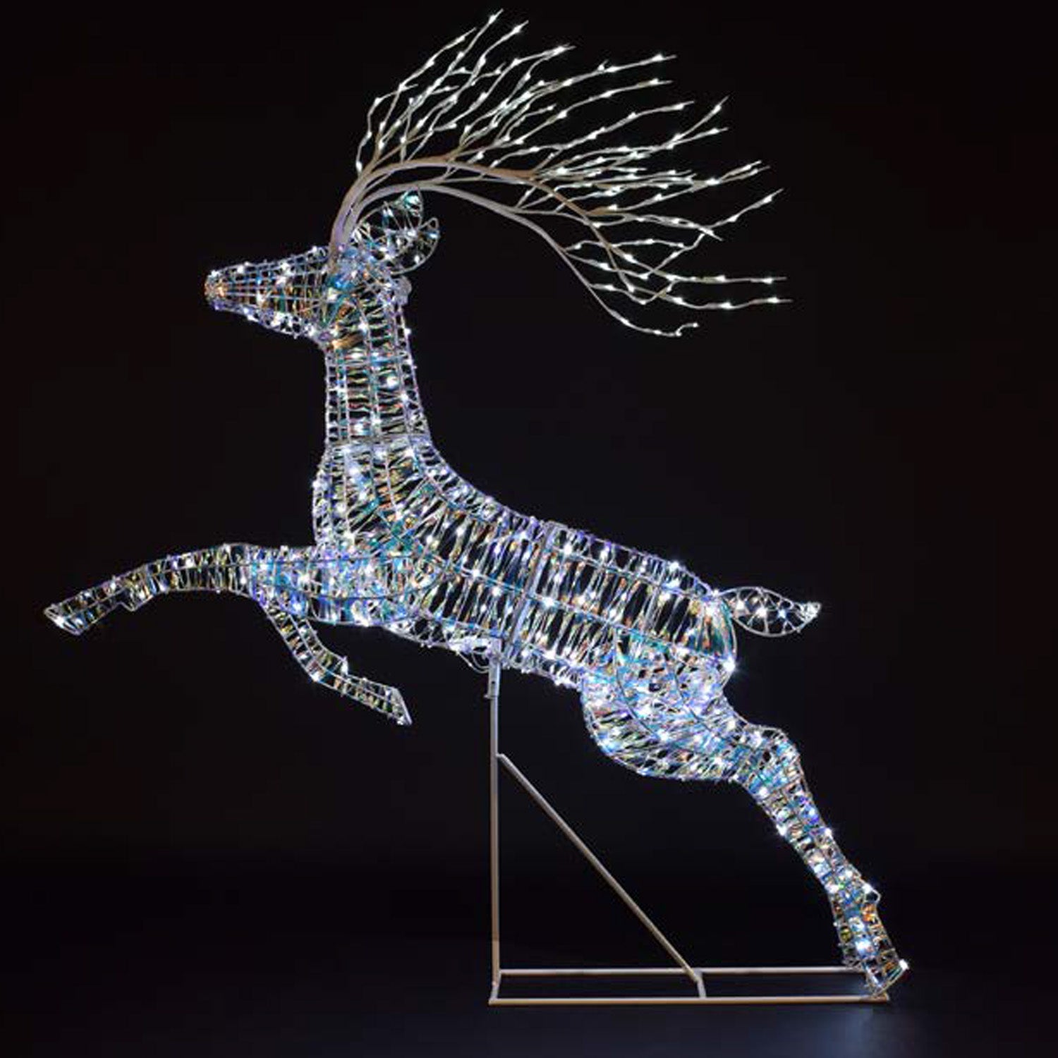 A leaping deer LED light decoration made of iridescent reflective segments, with branching antlers lit by small white lights, standing on a metal support against a black background.