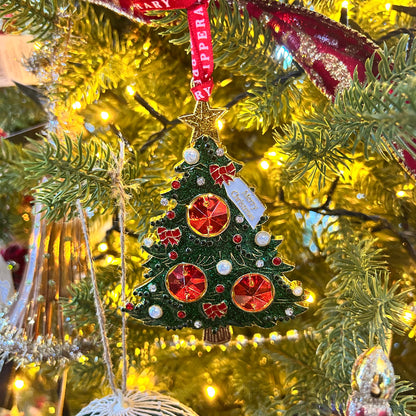 Decorative Christmas tree ornament with red and gold details hanging on a lit Christmas tree.