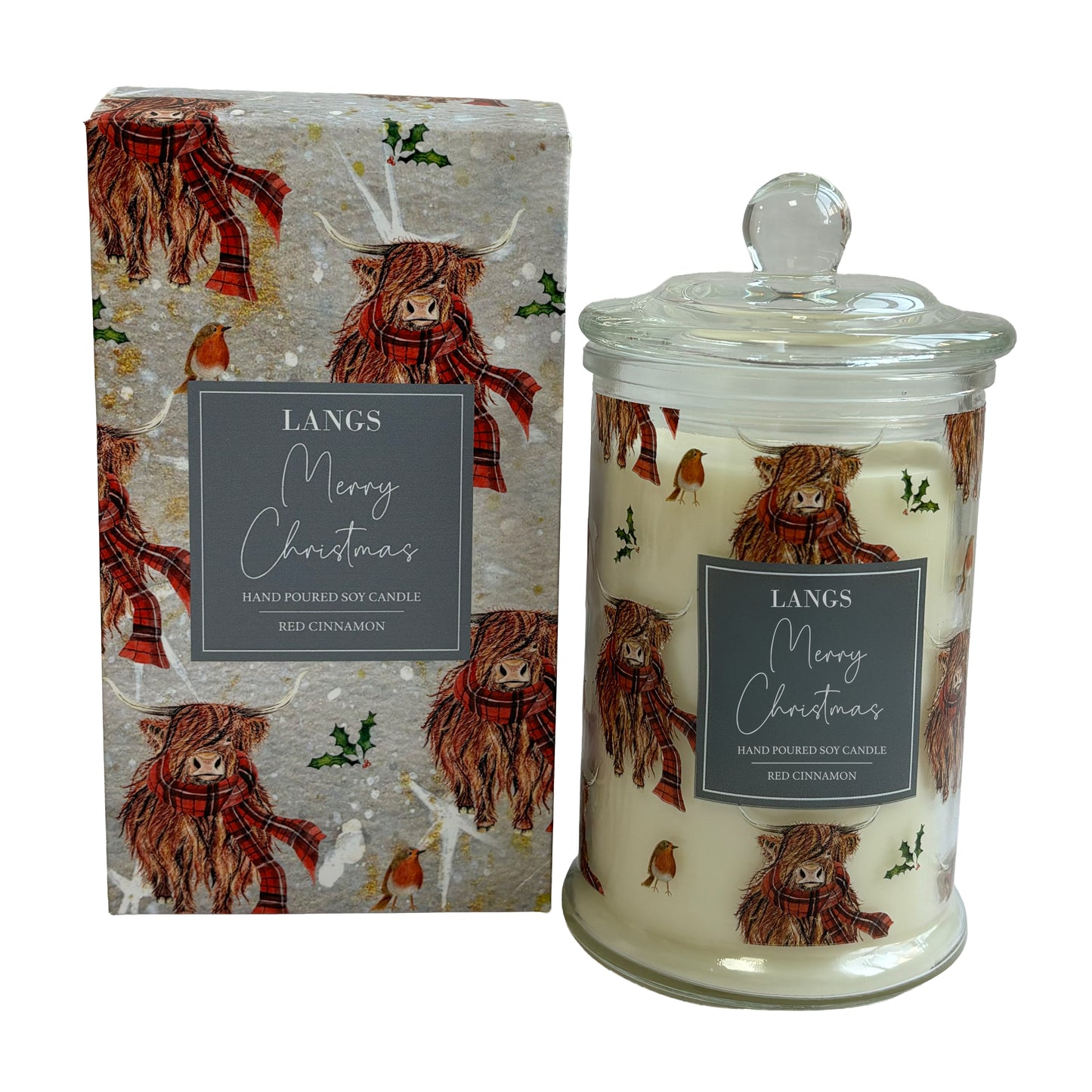 A hand-poured soy candle in a clear glass jar with a glass lid, shown next to its illustrated packaging box. The candle and box feature a festive Christmas design with Highland cows wearing red plaid scarves, set against a light gray background with gold glitter and green holly accents.