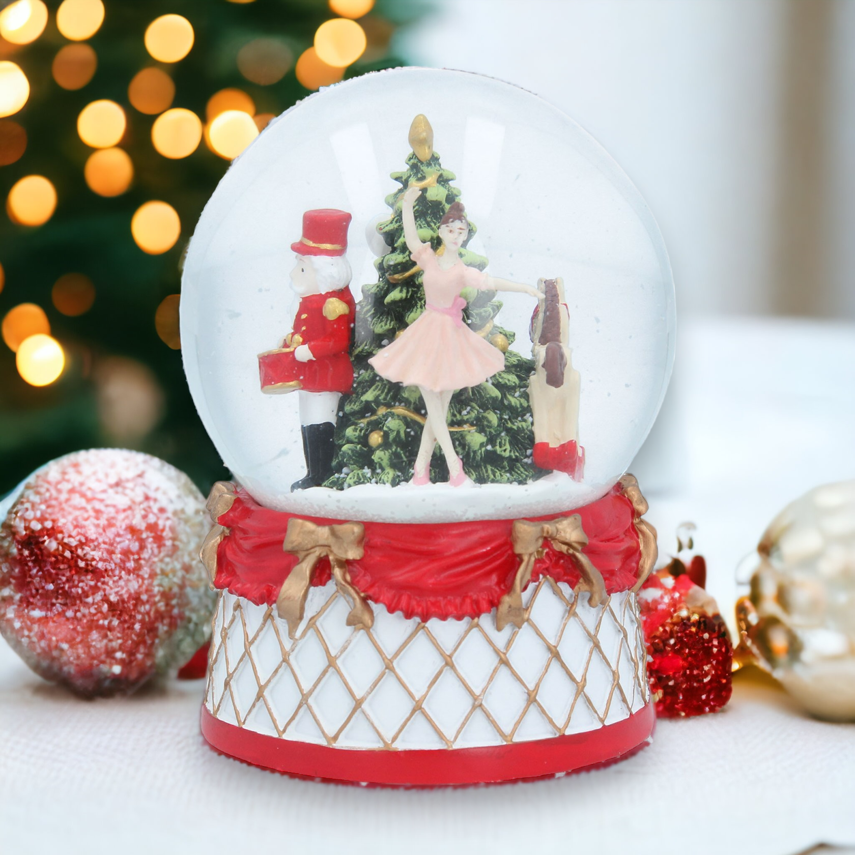 A musical Christmas snow globe featuring a nutcracker and a ballerina figure around a Christmas tree, placed on a decorated base with festive ornaments around.