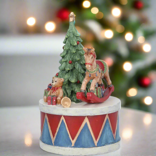 A decorative music box featuring a teddy bear rocking horse and a Christmas tree with gifts, set against a festive background with Christmas lights.