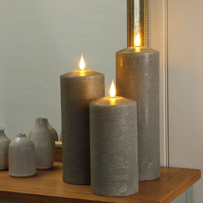 Three grey textured pillar candles with lit flames are arranged on a wooden cabinet next to small white ribbed vases in front of a mirror.