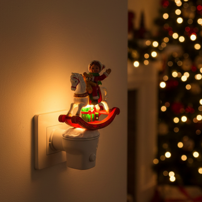 A Christmas-themed night light plug-in on a wall, featuring a rocking horse with a child rider and glowing green gifts, with a blurred Christmas tree in the background.