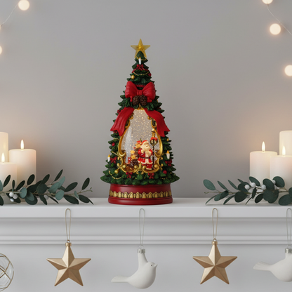A decorative Christmas tree figurine water spinner with Santa Claus and a snow globe inside, displayed on a white mantelpiece with lit candles, greenery, and hanging star ornaments in the background.