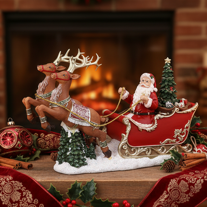A festive Christmas ornament or figurine featuring Santa Claus in a red sleigh pulled by two brown reindeer, with small decorated trees and holiday greenery, displayed in front of a blurred fireplace.