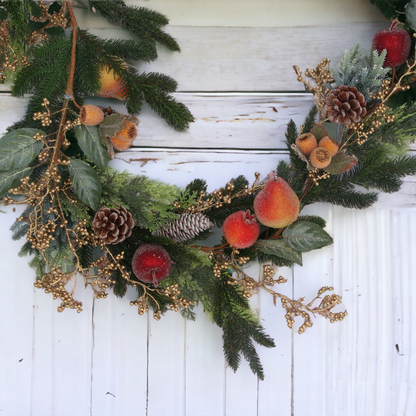 A decorative Christmas garland featuring a variety of artificial fruits, pinecones, and gold-colored branches, wreathed together on a white fence.