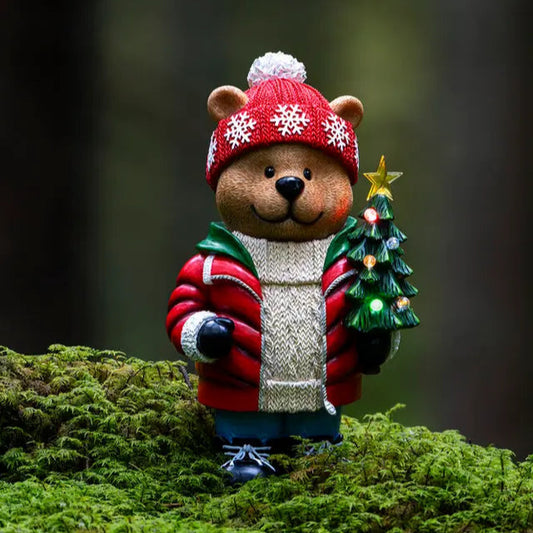 A decorative teddy bear wearing a Christmas hat and holding a miniature Christmas tree, placed on a mossy surface.