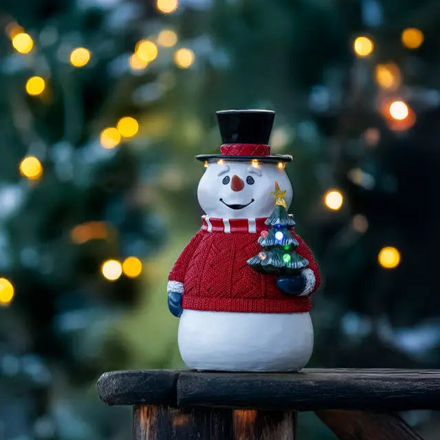 Decorative snowman figurine with a tree on a wooden surface at night.
