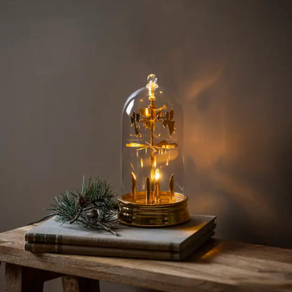 Decorative lamp with glowing interior on books under a glass dome.