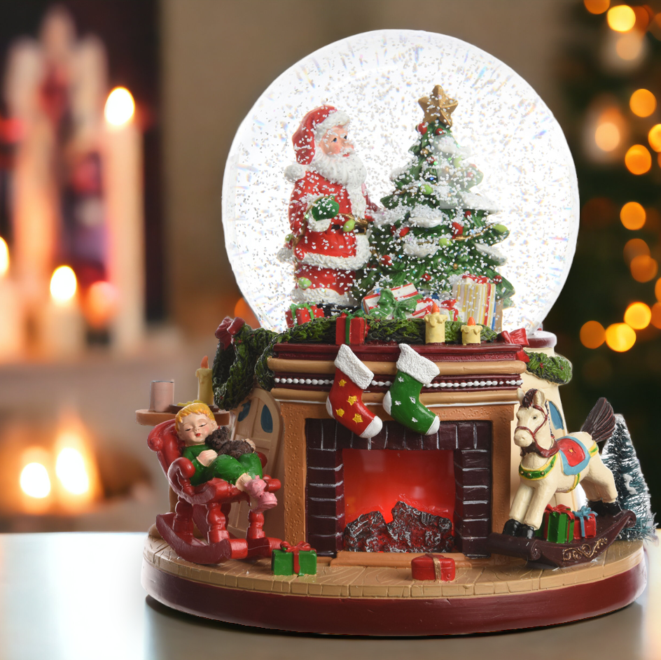 A Christmas-themed snowglobe featuring a fireplace scene with Santa Claus, a Christmas tree, and holiday gifts inside the globe. The base is brown, and there is a blurred warm light background.