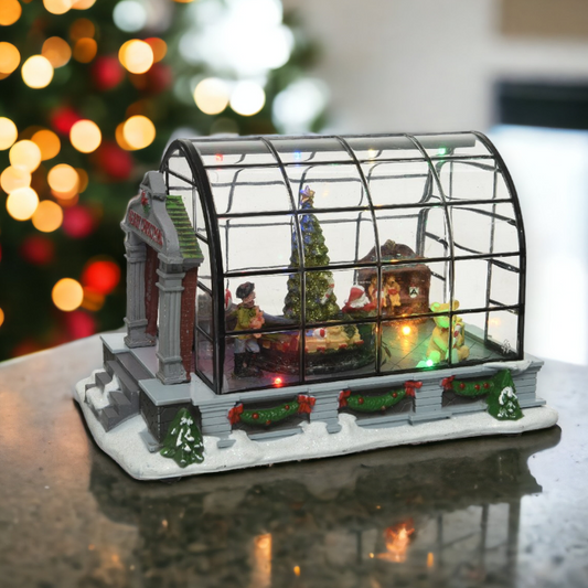 A Christmas greenhouse decoration featuring a revolving Santa tree and train, with vintage style figures, set against a blurred holiday-themed backdrop.
