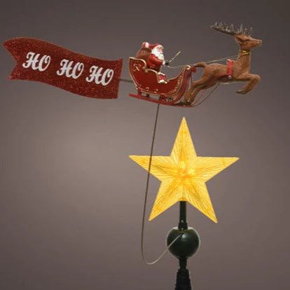 Decorative Christmas topper with Santa Claus in sleigh, reindeer, and 'HO HO HO' banner on a gray background.